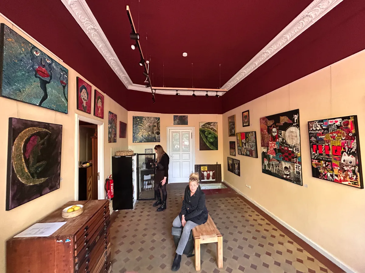 Inside the gallery: paintings hung close together on the burgundy walls, an upright piano in the corner